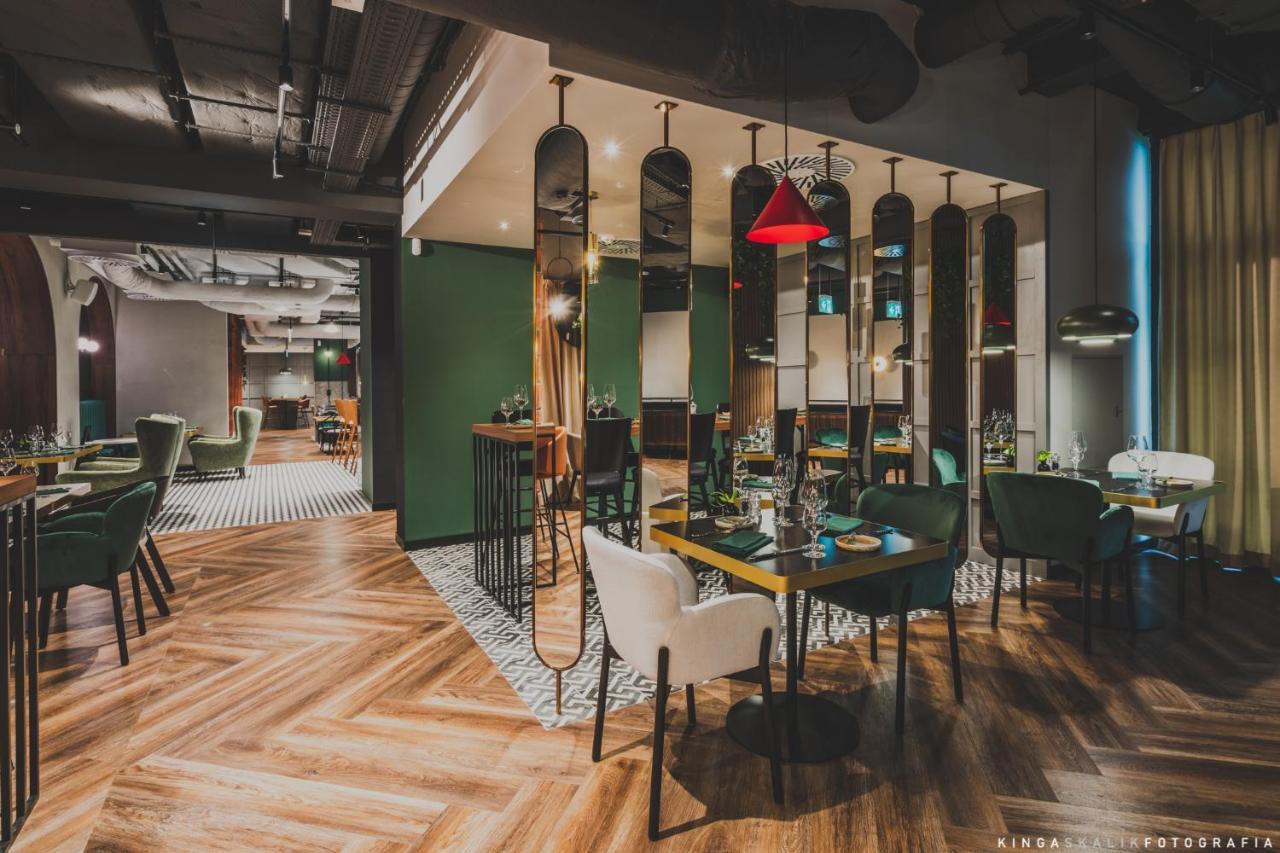 Апарт отель Royal Tulip Warsaw Centre Экстерьер фото The image depicts a modern restaurant interior. It features a combination of stylish furniture, including green and white chairs around wooden tables. The floor has a distinctive herringbone pattern, and there are mirrors along the walls, adding dept