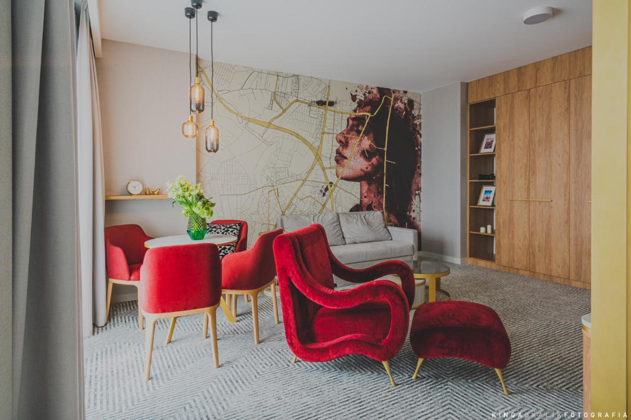 Апарт отель Royal Tulip Warsaw Centre Экстерьер фото The photo shows a stylish and modern living space. The room features a large wall mural depicting a woman's face, which adds an artistic touch. In the foreground, there are several red armchairs with a plush design, complemented by a small round tabl