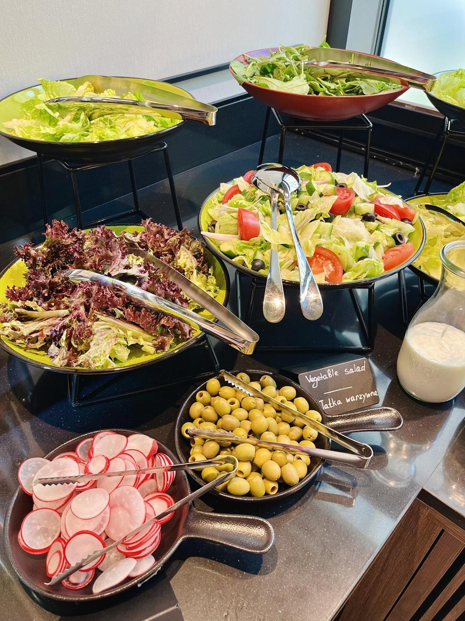 Апарт отель Royal Tulip Warsaw Centre Экстерьер фото The photo shows a variety of salad options arranged on a table. 

1. **Salads**: There are two larger bowls—one with mixed greens, including red leaf lettuce, and another with a colorful salad that includes chopped tomatoes, cucumbers, and olives.
2.
