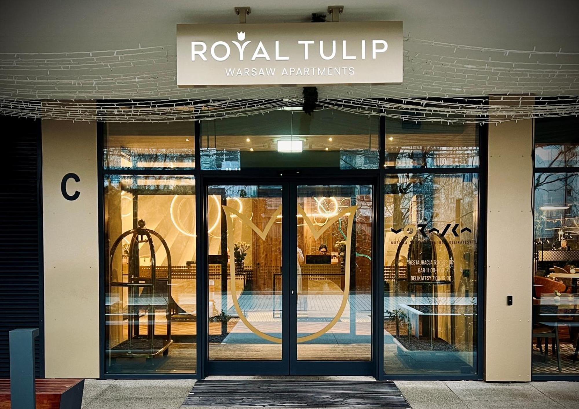 Апарт отель Royal Tulip Warsaw Centre Экстерьер фото The photo shows the entrance to a hotel named "Royal Tulip." The facade features large glass doors that allow a view into the lobby area. There are decorative elements, including what appears to be luggage carts near the entrance. Above the doors is 