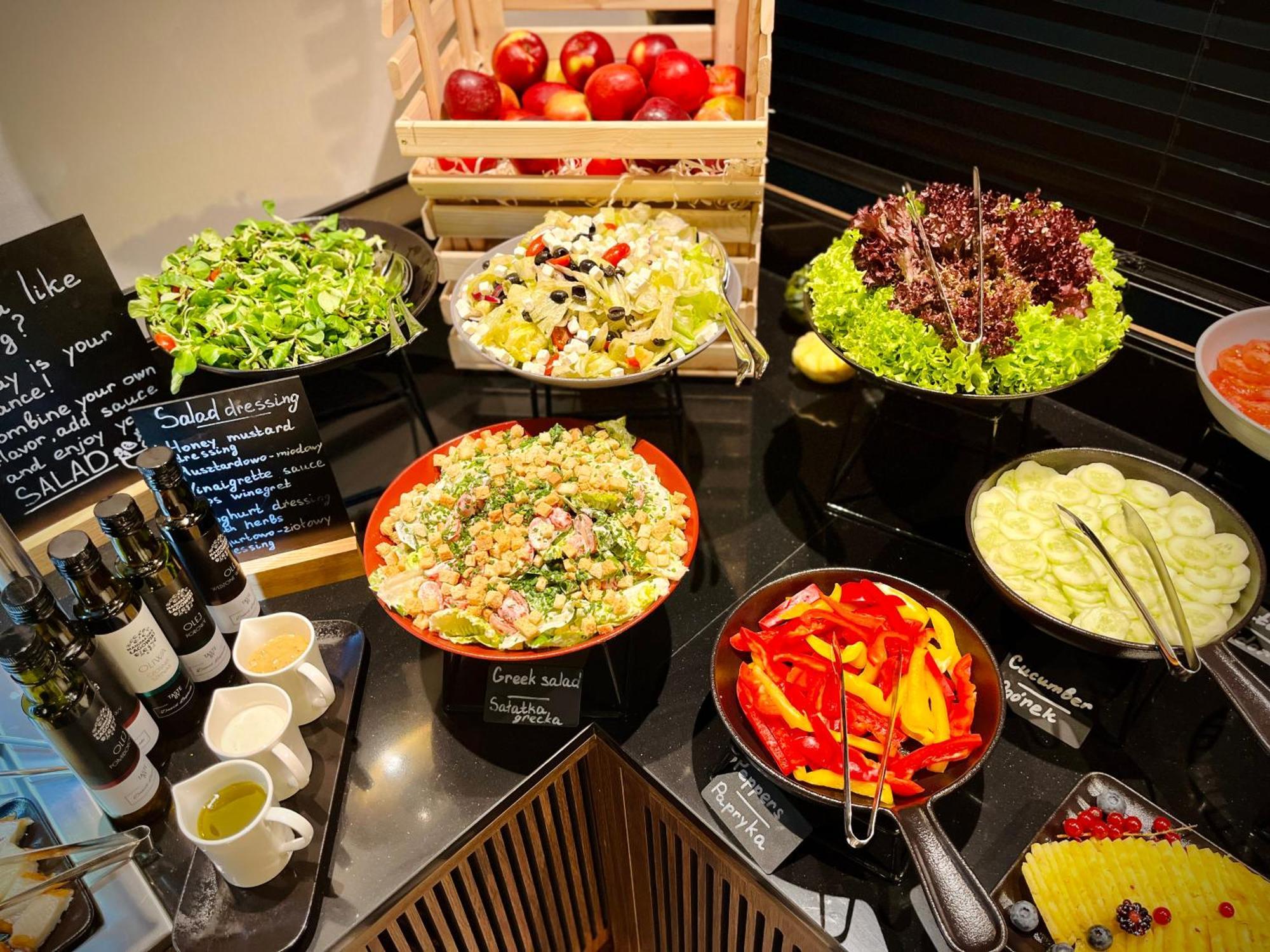 Апарт отель Royal Tulip Warsaw Centre Экстерьер фото The photo shows a well-arranged salad bar featuring a variety of fresh salads and ingredients. There are several bowls and dishes with different types of salads, including green salads and grain salads. 

1. **Green Salads**: There are multiple bowls